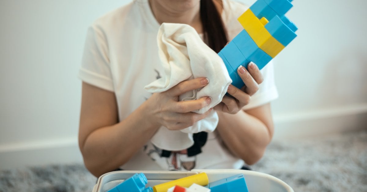 A person is sitting in a room while wiping a blue and yellow building-block toy using a white cloth.